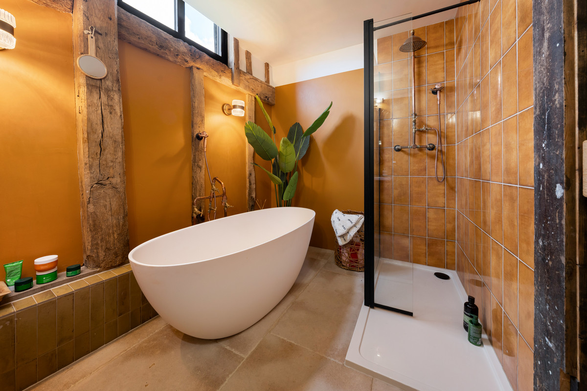 Barn Owl bathroom with ochre walls, a freestanding white bath and exposed timber beams
