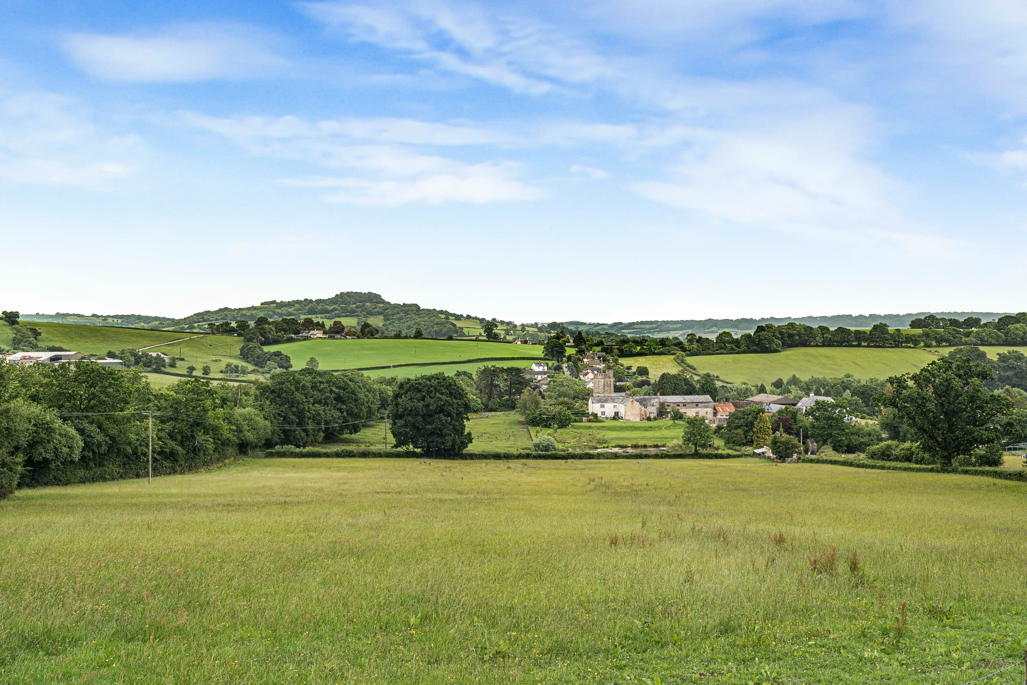 Green countryside, fields and a village church beneath a blue sky
